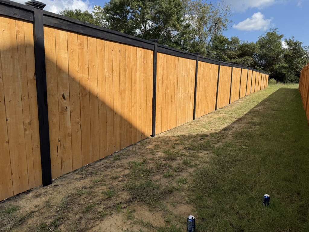 Newly installed wooden privacy fence with black posts in sunny backyard.