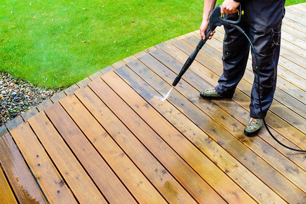 Man pressure washing wooden deck for cleaning and maintenance.